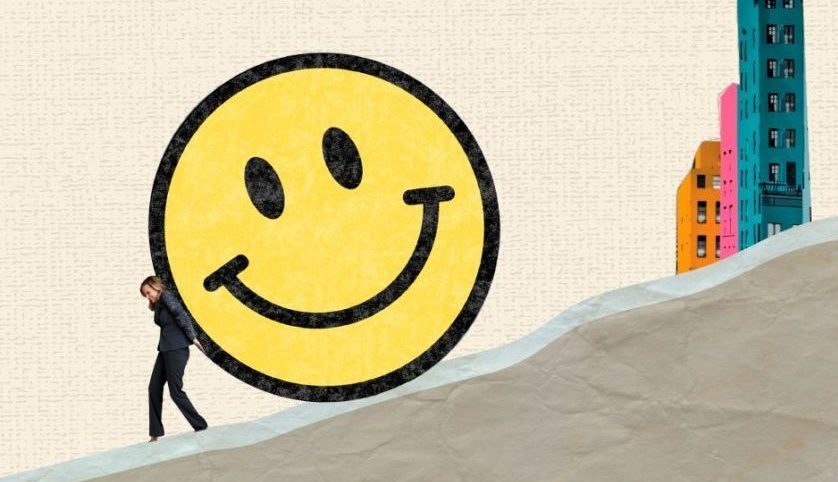 A person pushes a big smiley face up a hill.